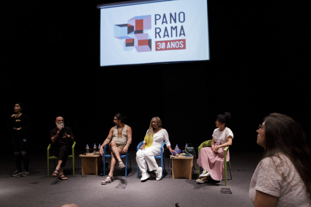 Imagem mostra participantes do seminário sentados lado a lado. Da esquerda para a direita: Marcelo Evelyn, Juão Nyn, Keyna Eleison e Camilla Rocha Campos