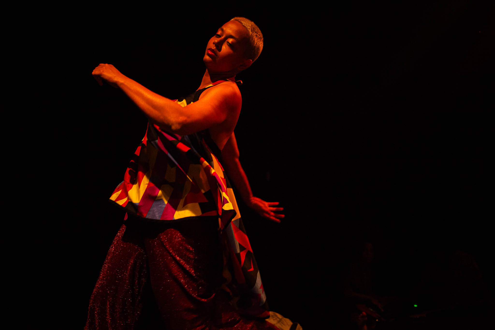 Laís Castro em performance sobre um palco escuro, vestindo figurino colorido e brilhante